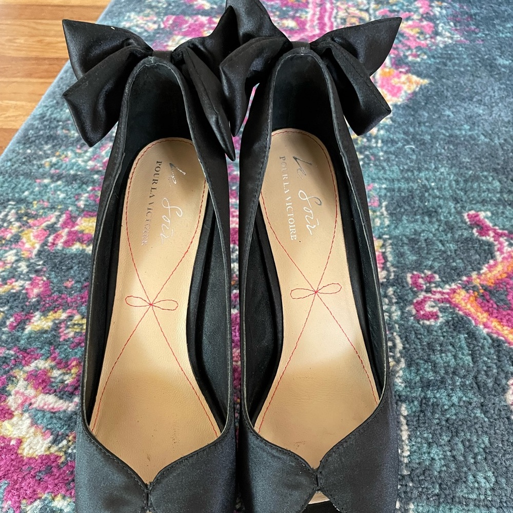 Pour La Victoire black satin peep toe pumps with bow on the heel.